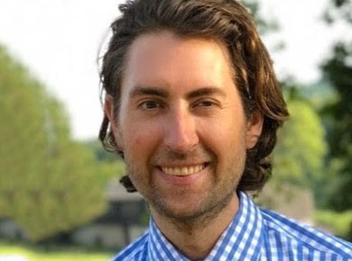 Headshot of James Tamplin outdoors wearing a blue checked shirt