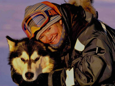 Photo of Sunniva Sorby in winter gear hugging a sled dog in the high Arctic